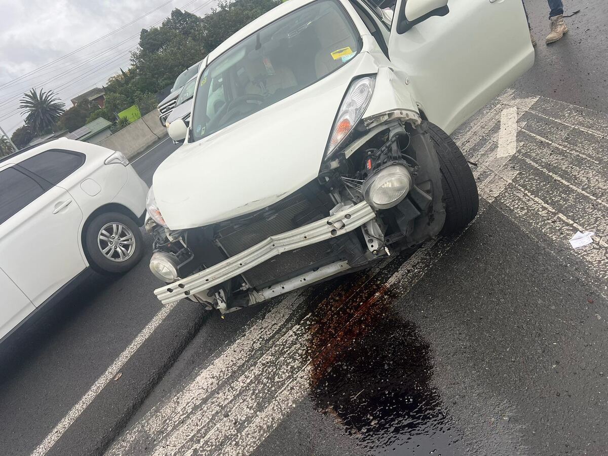 White car with front suspension and wheel damage after a crash, leaking fluid on the road